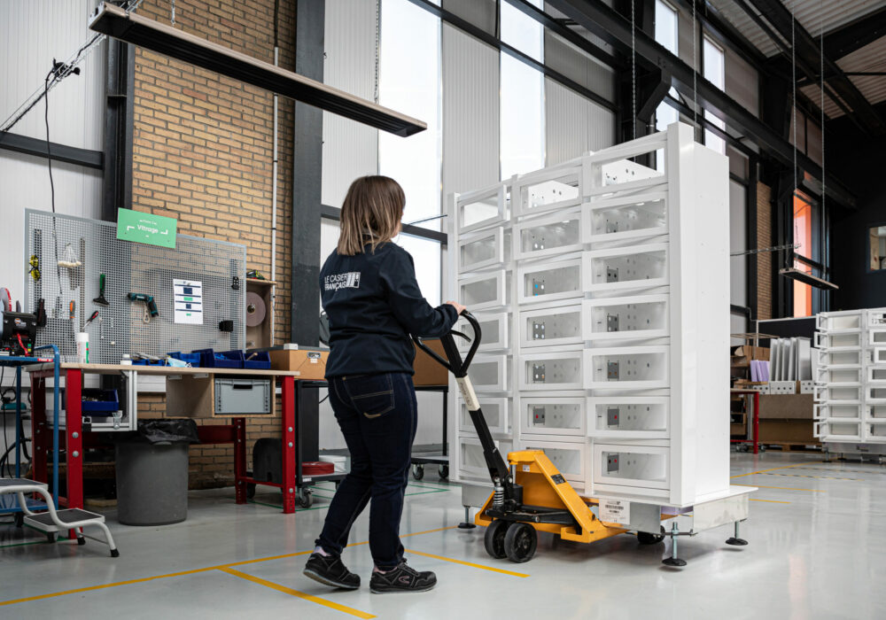Technicienne Le Casier Français chargeant un distributeur automatique sur un transpalette pour le passer à l'étape de fabrication suivante