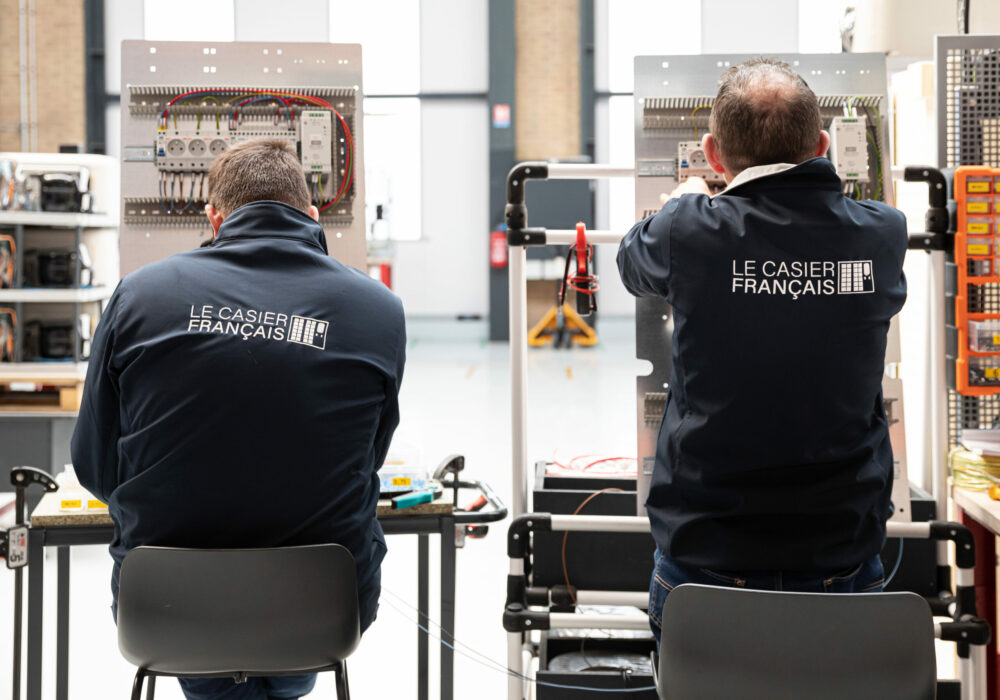 2 techniciens Le Casier Français de dos en train de monter les blocs électriques pour le prochain distributeur automatique