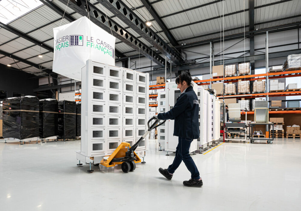 Technicienne Le Casier Français en charge de déplacer un distributeur automatique en cours de fabrication